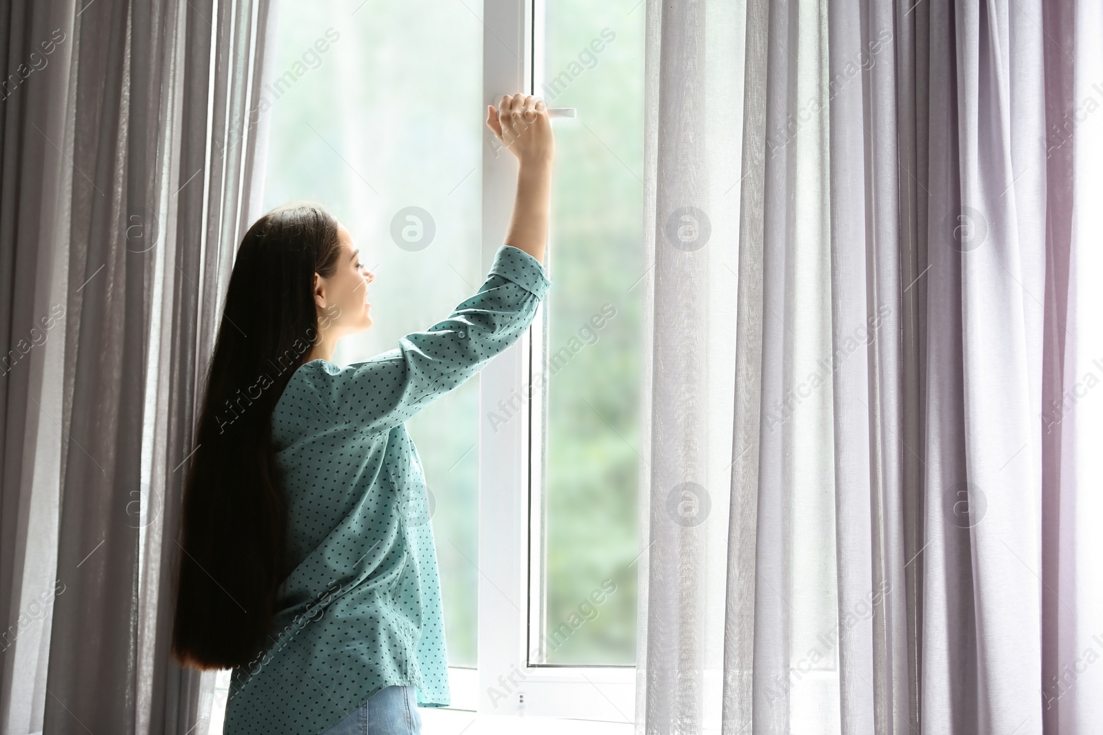 Photo of Young beautiful woman opening big window in room