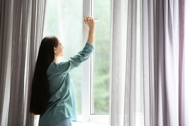 Photo of Young beautiful woman opening big window in room