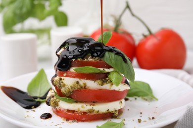 Photo of Pouring balsamic vinegar onto stacked Caprese salad with pesto sauce on table, closeup