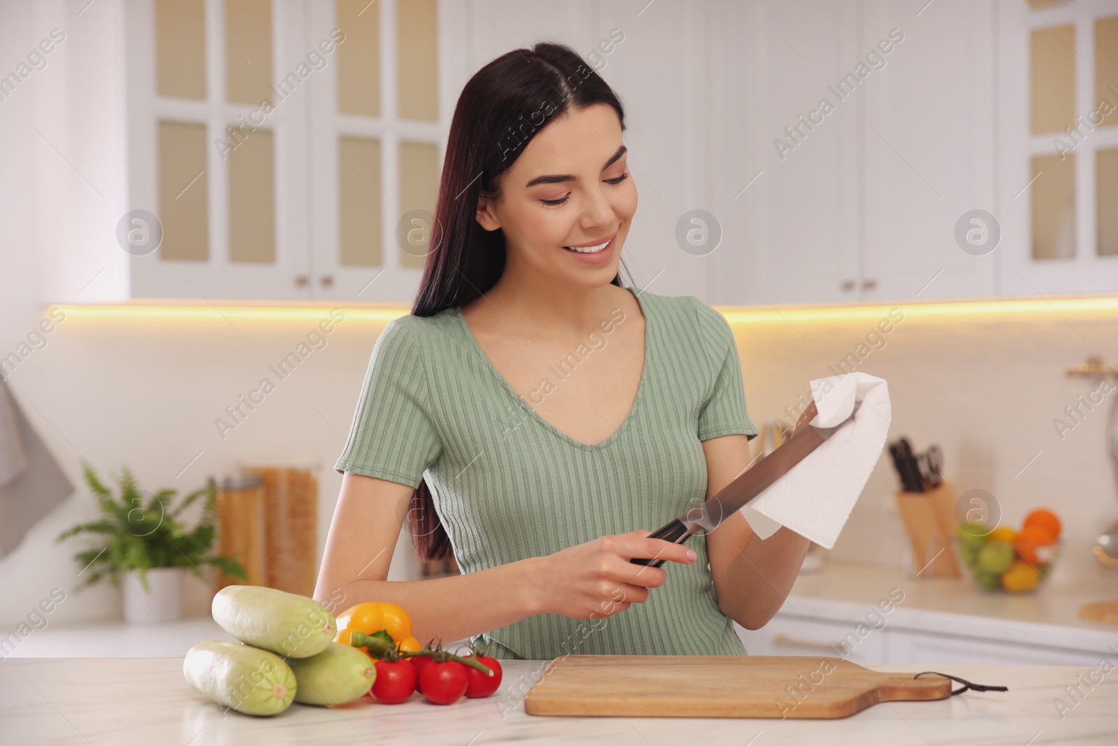 Photo of Woman wiping knife with paper towel in kitchen