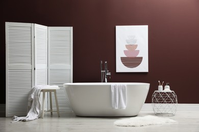 Photo of Modern ceramic bathtub and furniture near burgundy wall in room