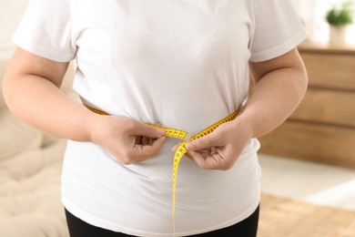 Photo of Overweight woman measuring waist with tape at home, closeup