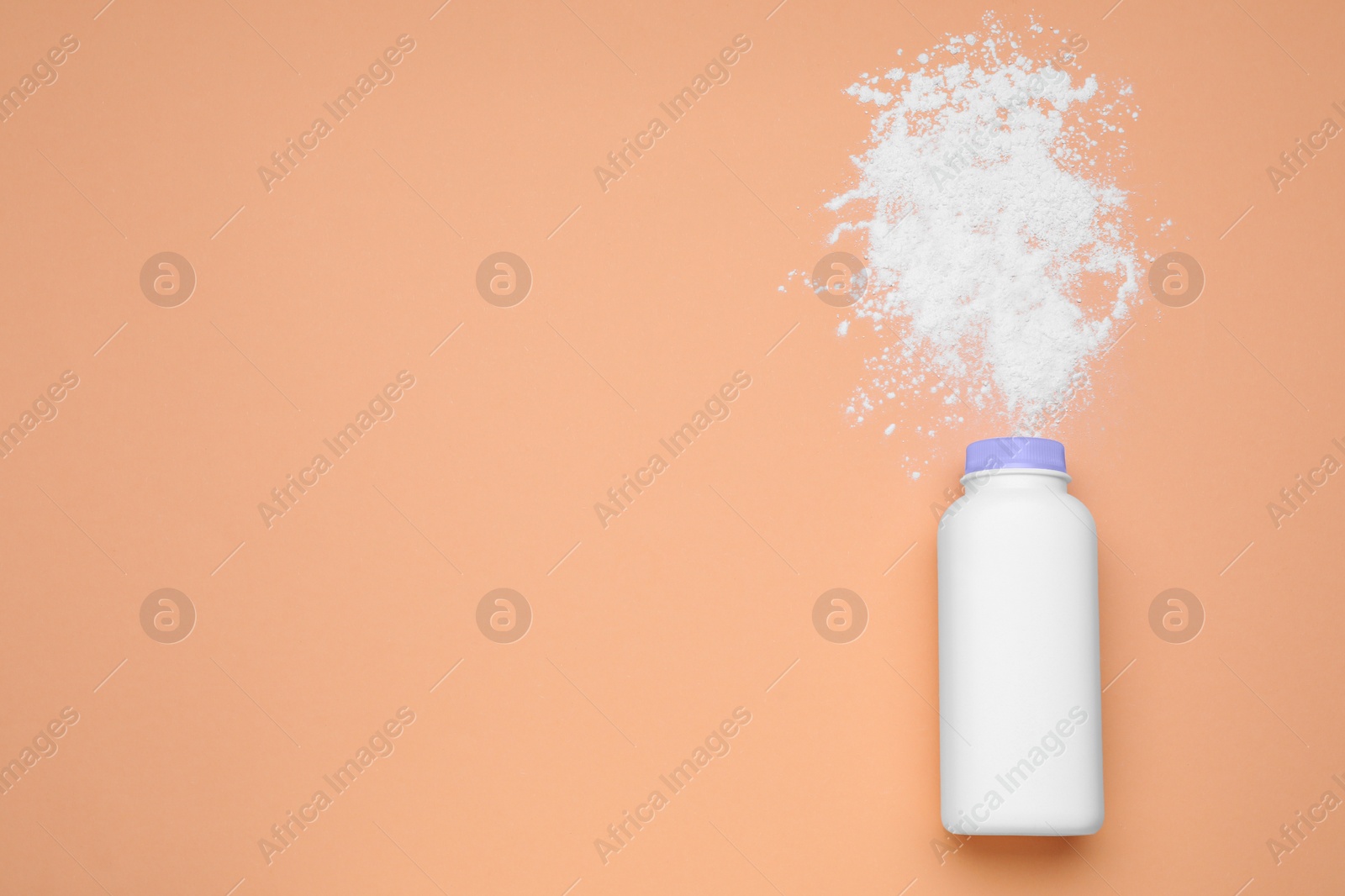 Photo of Bottle and scattered dusting powder on pale coral background, top view with space for text. Baby cosmetic product