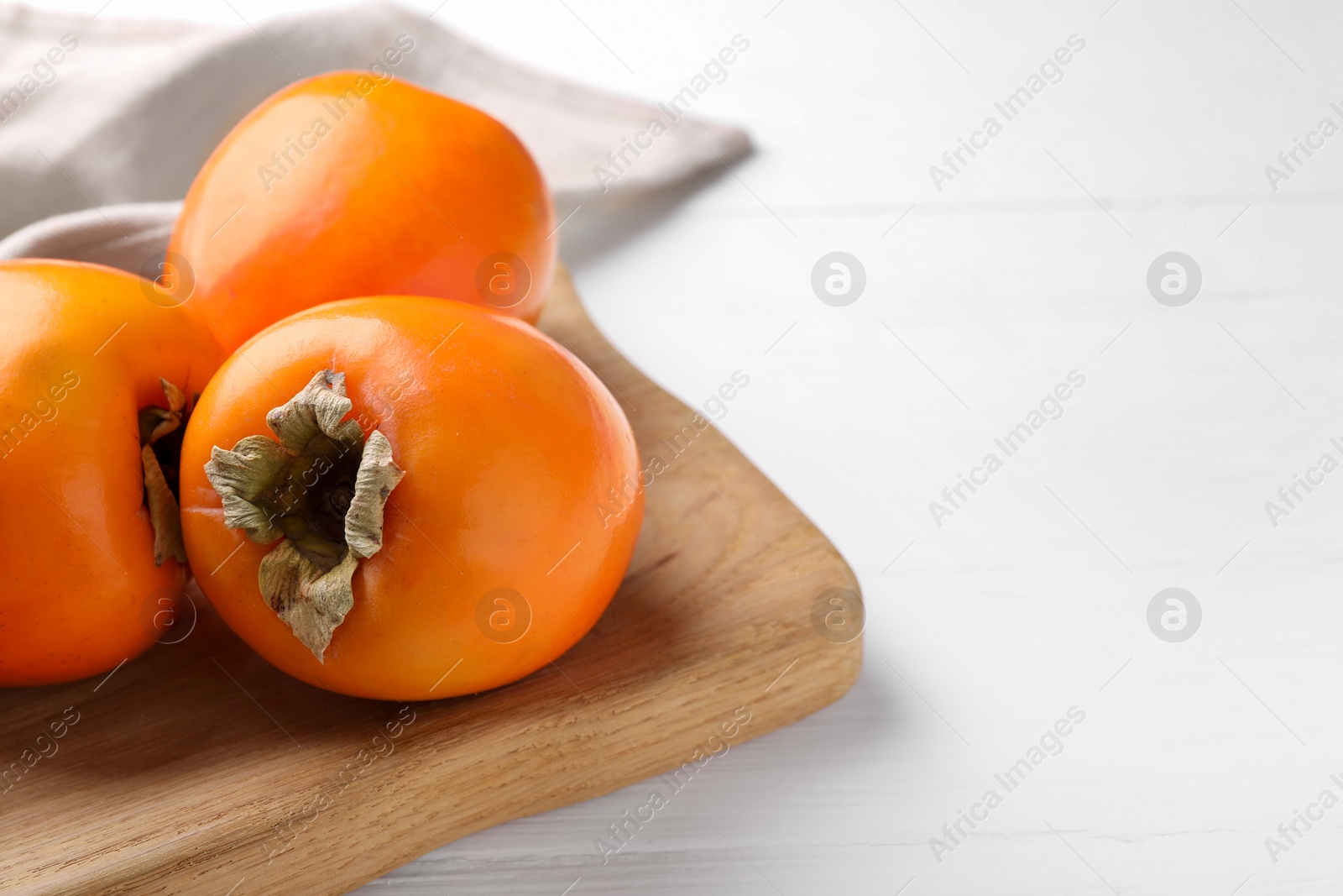 Photo of Board with delicious ripe persimmons on white wooden table, closeup. Space for text