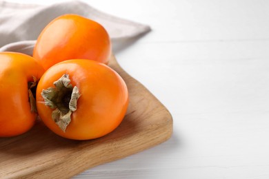 Photo of Board with delicious ripe persimmons on white wooden table, closeup. Space for text