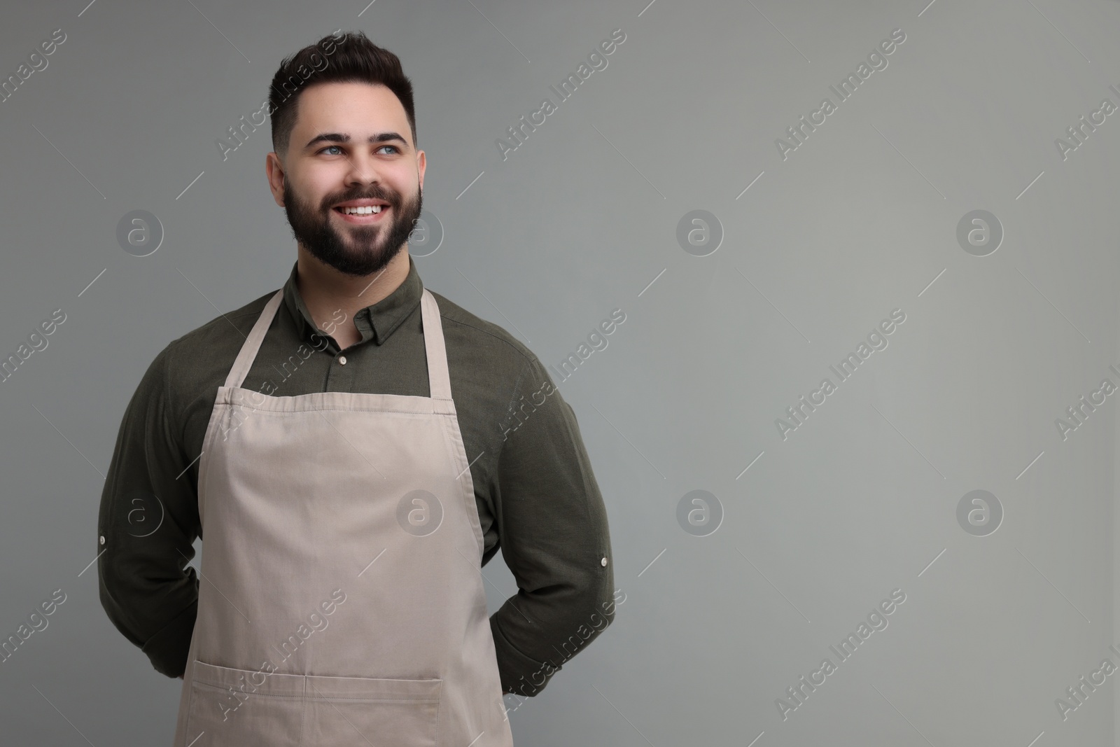 Photo of Smiling man in kitchen apron on grey background. Mockup for design