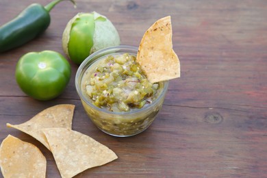 Tasty salsa sauce, ingredients and tortilla chips on wooden table, closeup. Space for text