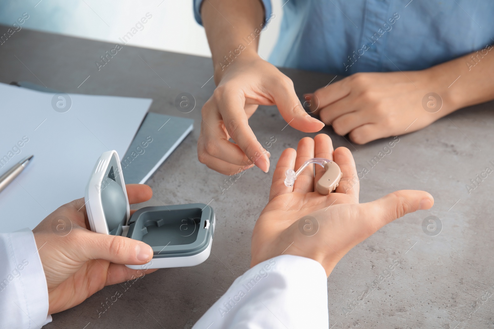 Photo of Doctor giving patient hearing aid at table in clinic, closeup