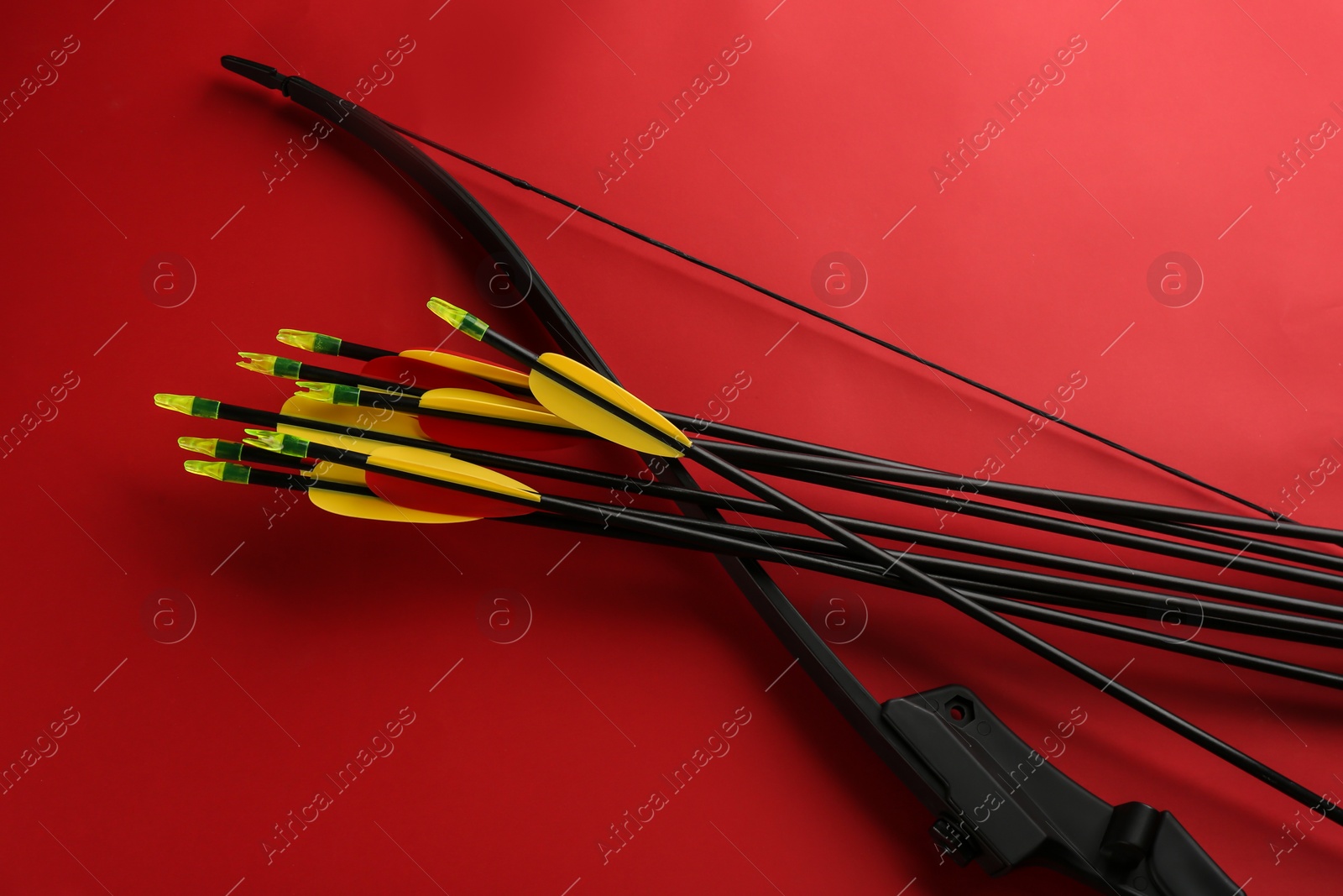 Photo of Black bow and set of arrows on red background, flat lay. Archery sports equipment