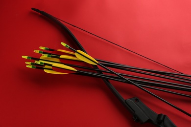 Photo of Black bow and set of arrows on red background, flat lay. Archery sports equipment