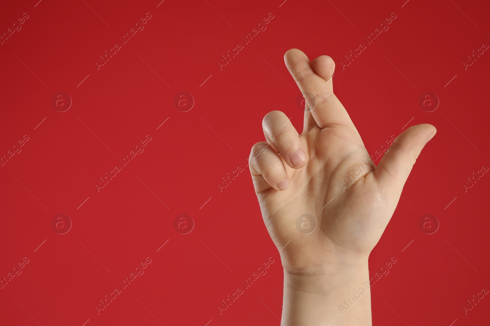 Photo of Child holding fingers crossed on red background, closeup with space for text. Good luck superstition