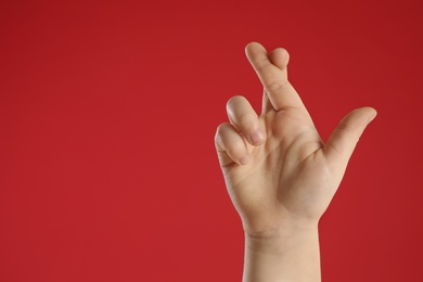 Child holding fingers crossed on red background, closeup with space for text. Good luck superstition