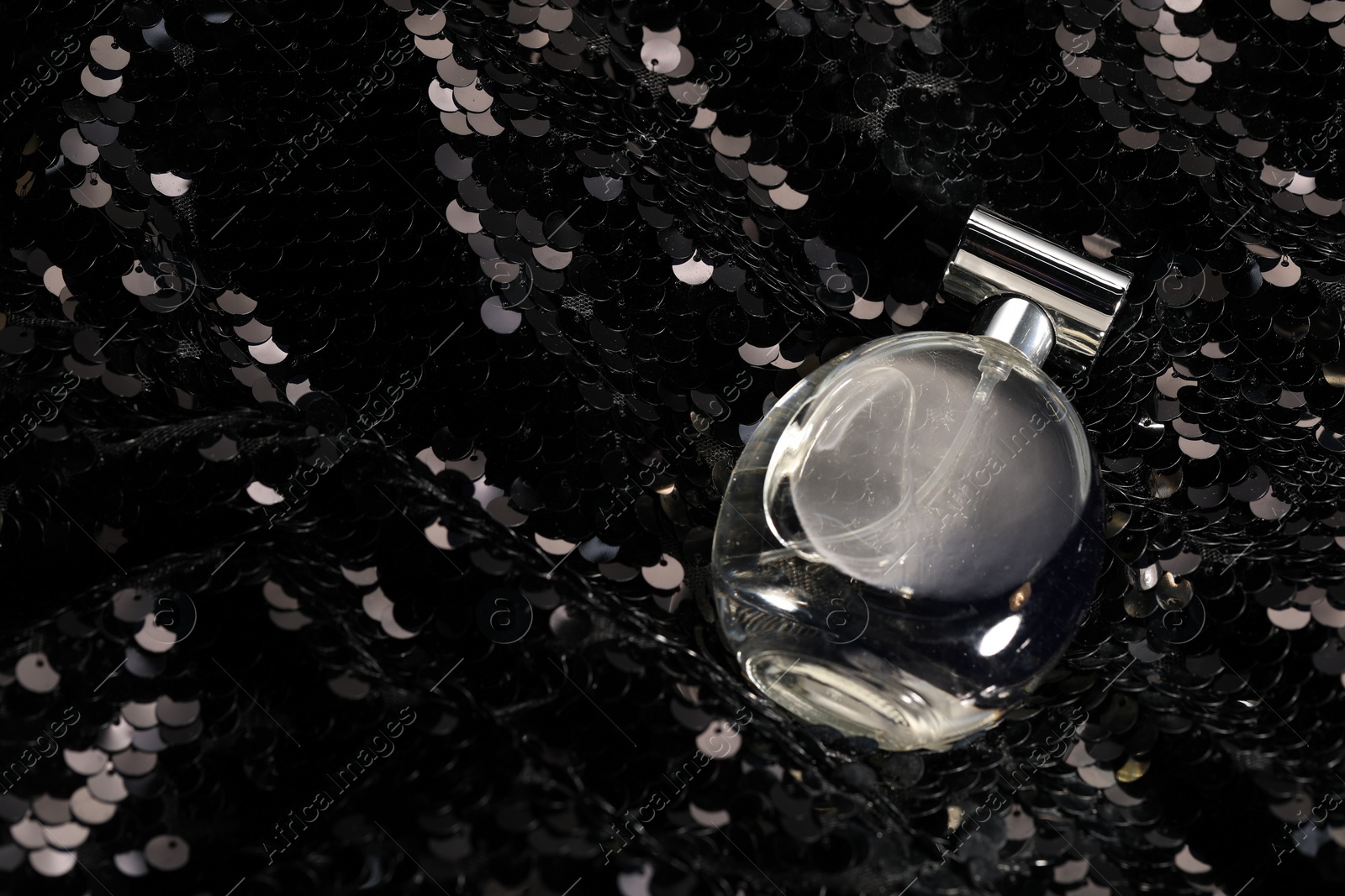 Photo of Luxury perfume in bottle on fabric with shiny sequins, above view