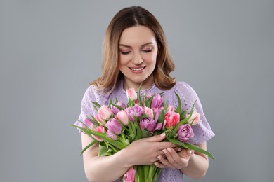 Photo of Happy young woman with bouquet of beautiful tulips on grey background