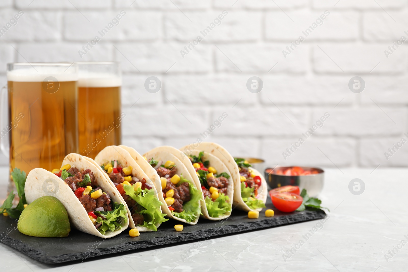 Photo of Delicious tacos with meat and vegetables on gray marble table against light brick wall, space for text