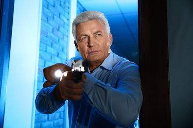 Photo of Professional security guard with gun and flashlight checking dark room