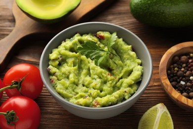 Photo of Delicious guacamole and ingredients on wooden table