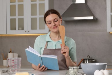 Photo of Happy woman with recipe book at table in kitchen