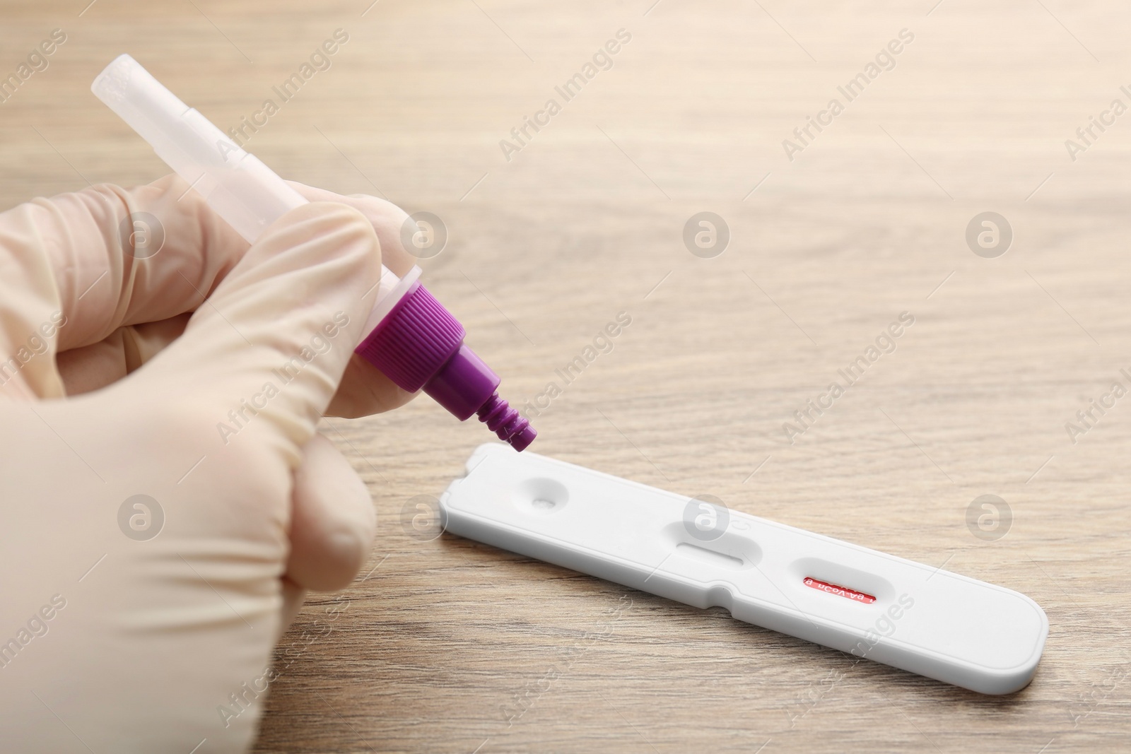 Photo of Doctor dropping buffer solution onto Covid-19 express test cassette at wooden table, closeup