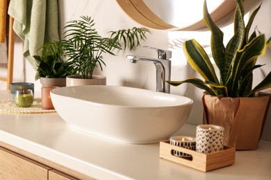 Photo of Bathroom counter with sink, candles and beautiful green houseplants near white marble wall