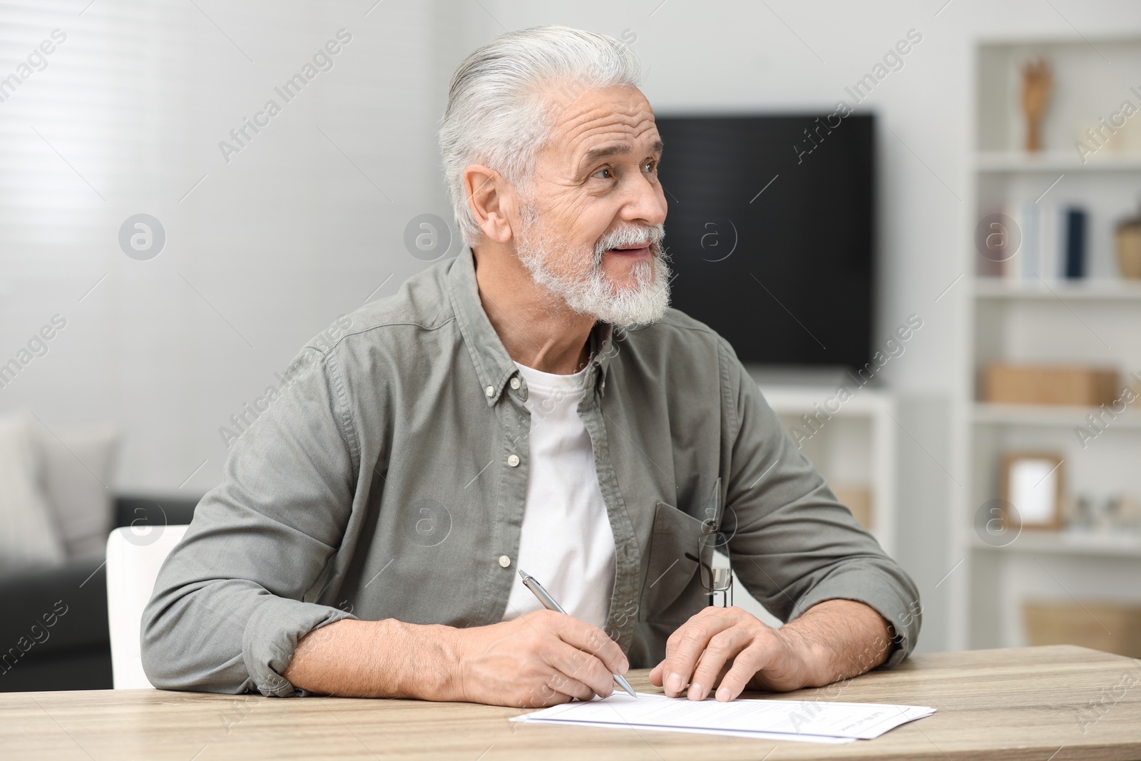 Photo of Senior man signing Last Will and Testament at table indoors