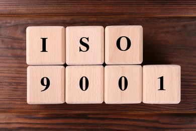 Photo of Cubes with abbreviation ISO and number 9001 on wooden table, flat lay