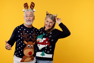 Photo of Senior couple in Christmas sweaters and reindeer headbands on orange background. Space for text