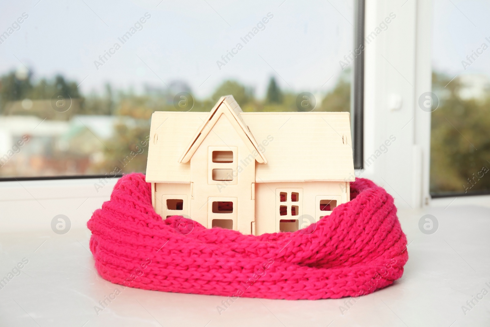 Photo of House model with knitted scarf on table against blurred background. Heating concept