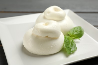 Photo of Delicious burrata cheese with basil on table, closeup