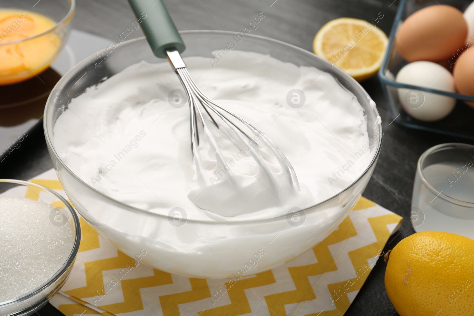 Photo of Bowl with whipped cream, whisk and ingredients on table, closeup