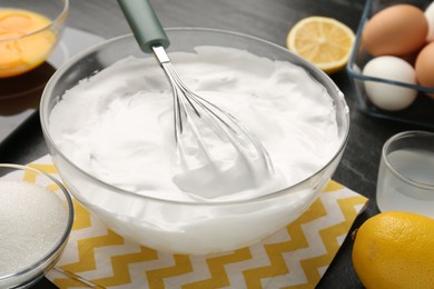 Bowl with whipped cream, whisk and ingredients on table, closeup