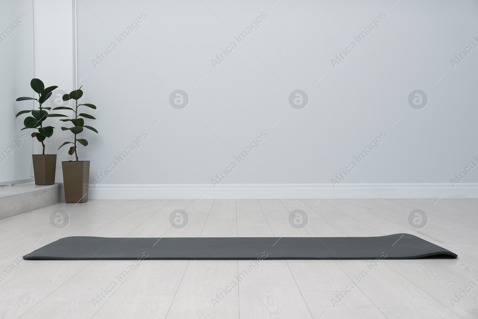 Photo of Unrolled black yoga mat on floor in room. Space for text