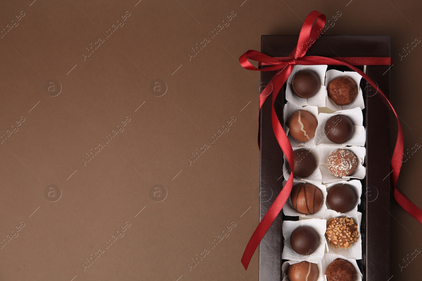 Photo of Box with delicious chocolate candies on brown table, top view. Space for text