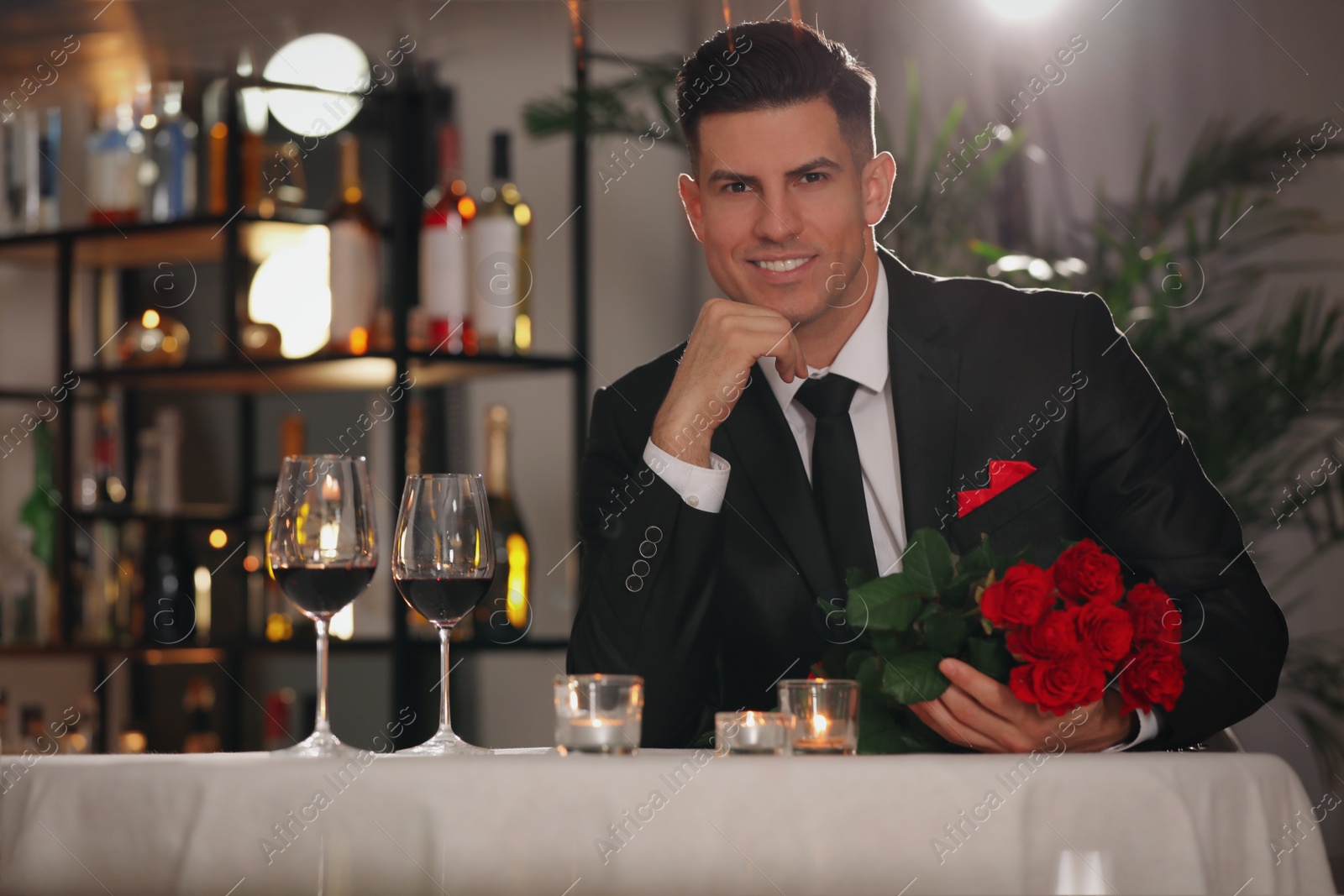 Photo of Happy man with roses waiting for his girlfriend in restaurant on Valentine's day