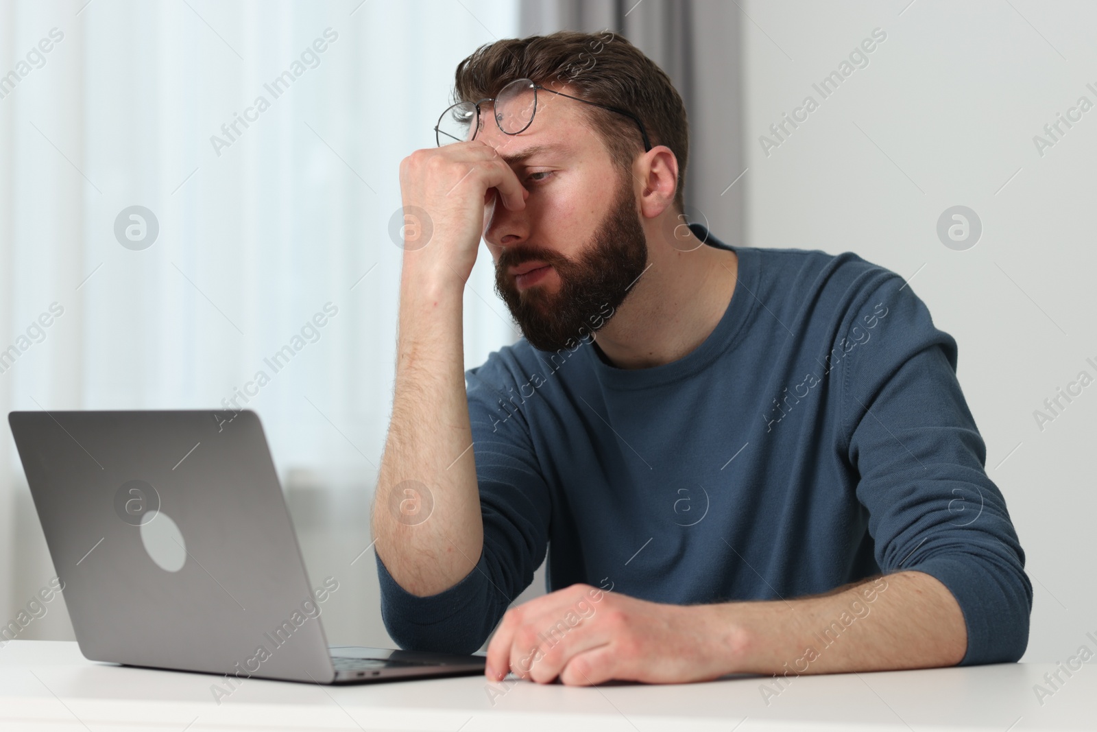 Photo of Overwhelmed man sitting with laptop at table indoors