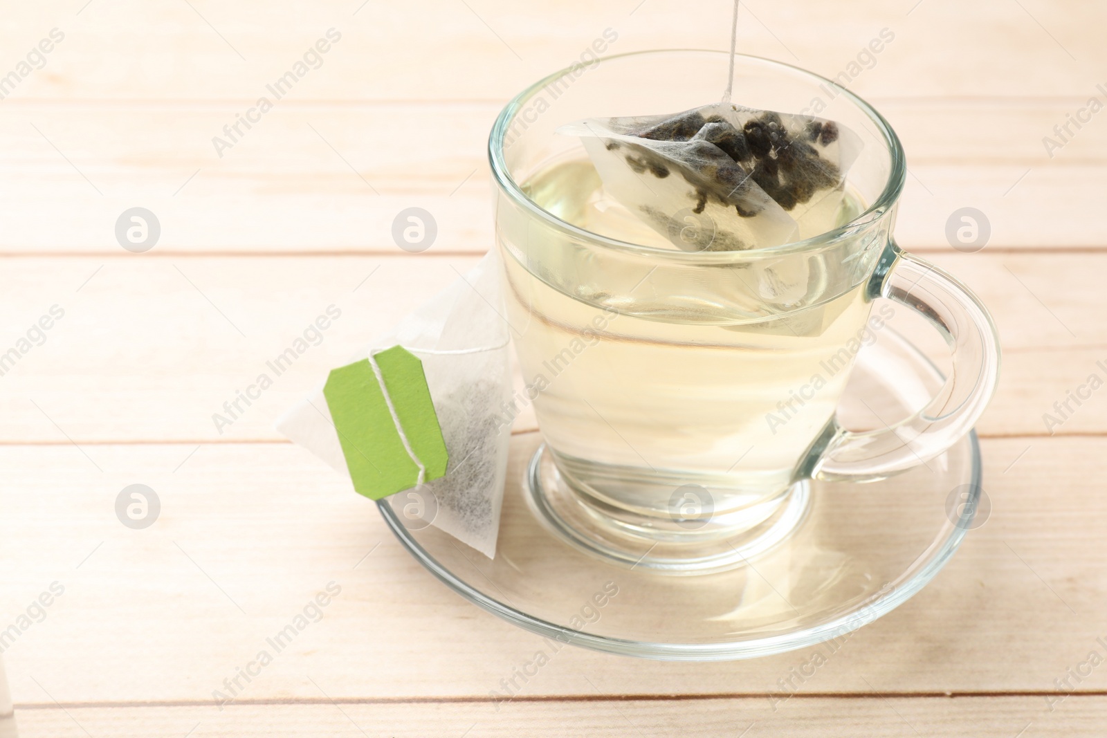 Photo of Putting tea bag in glass cup on light wooden table, closeup. Space for text