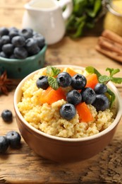 Tasty millet porridge with blueberries, pumpkin and mint in bowl on wooden table, closeup