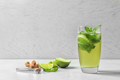 Photo of Glass with aromatic mint tea, fresh leaves, lime and sugar cubes on table