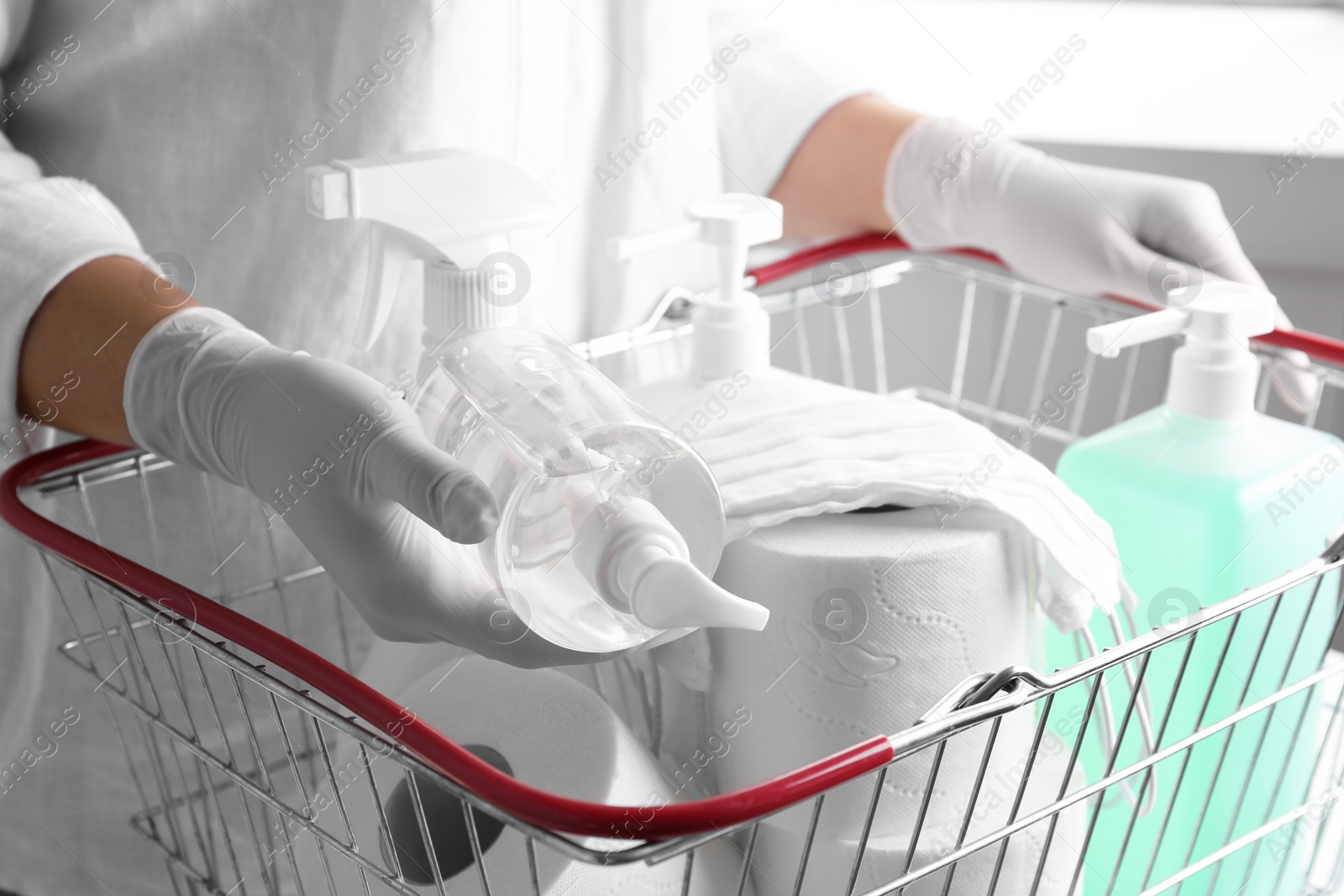 Photo of Woman with shopping basket full of antiseptics and toilet paper, closeup. Panic caused by virus