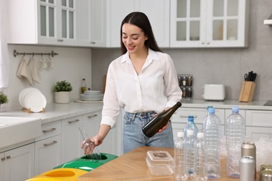 Photo of Garbage sorting. Smiling woman with glass bottles in kitchen