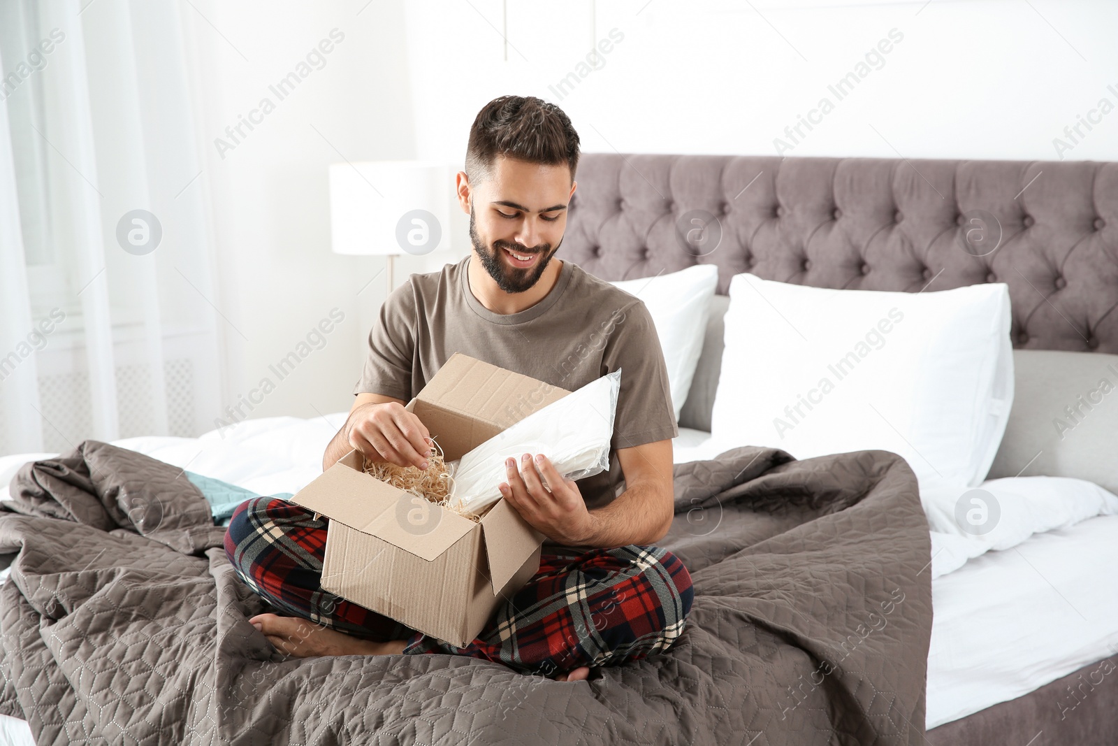 Photo of Young man opening parcel in bedroom at home