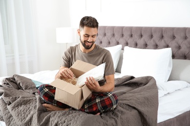 Young man opening parcel in bedroom at home