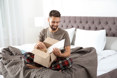 Photo of Young man opening parcel in bedroom at home