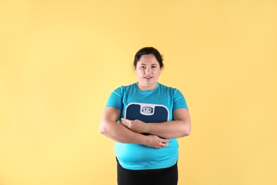 Overweight woman in sportswear with scales on color background