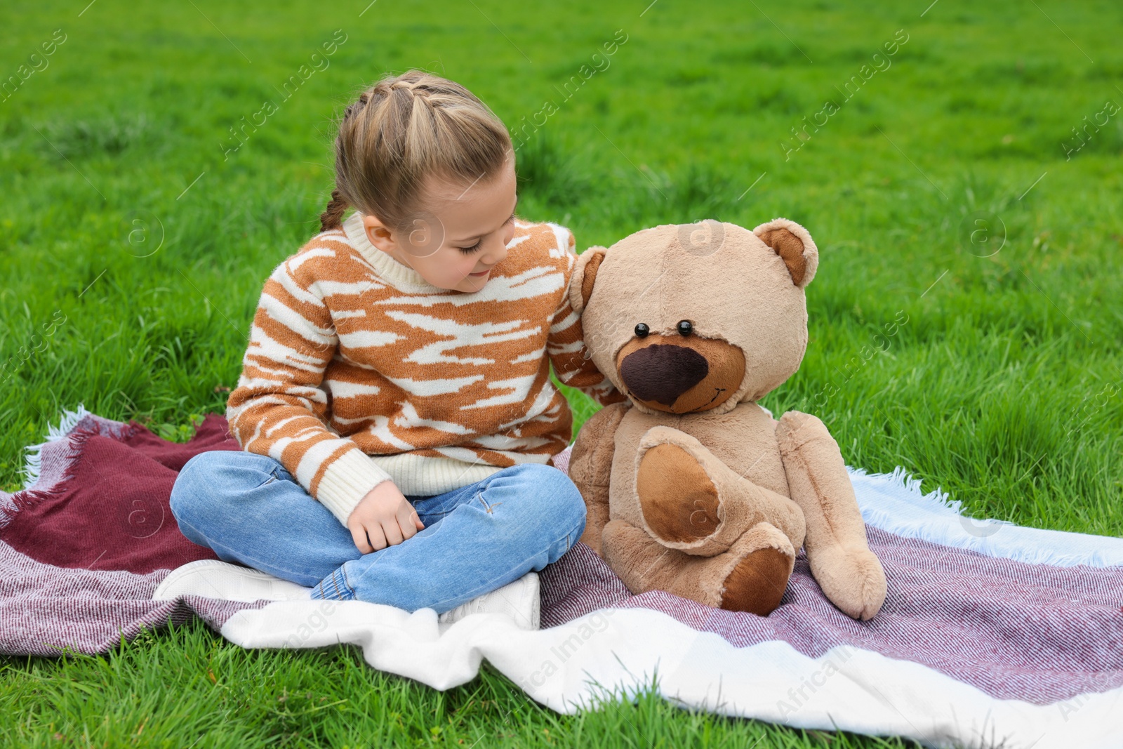 Photo of Little girl with teddy bear on plaid outdoors