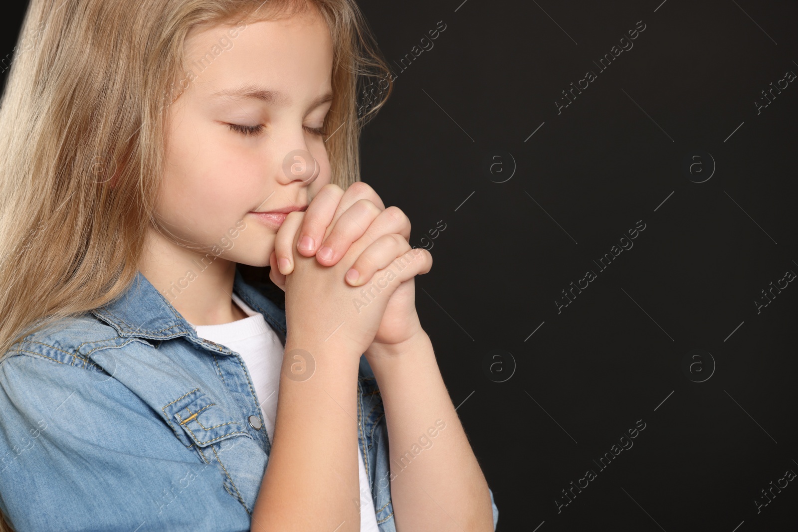 Photo of Girl with clasped hands praying on black background, space for text