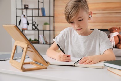 Boy in earphones doing homework at table indoors