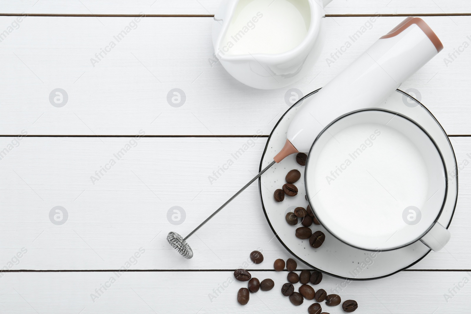 Photo of Flat lay composition with mini mixer (milk frother), whipped milk and coffee beans on white wooden table. Space for text