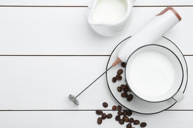 Flat lay composition with mini mixer (milk frother), whipped milk and coffee beans on white wooden table. Space for text