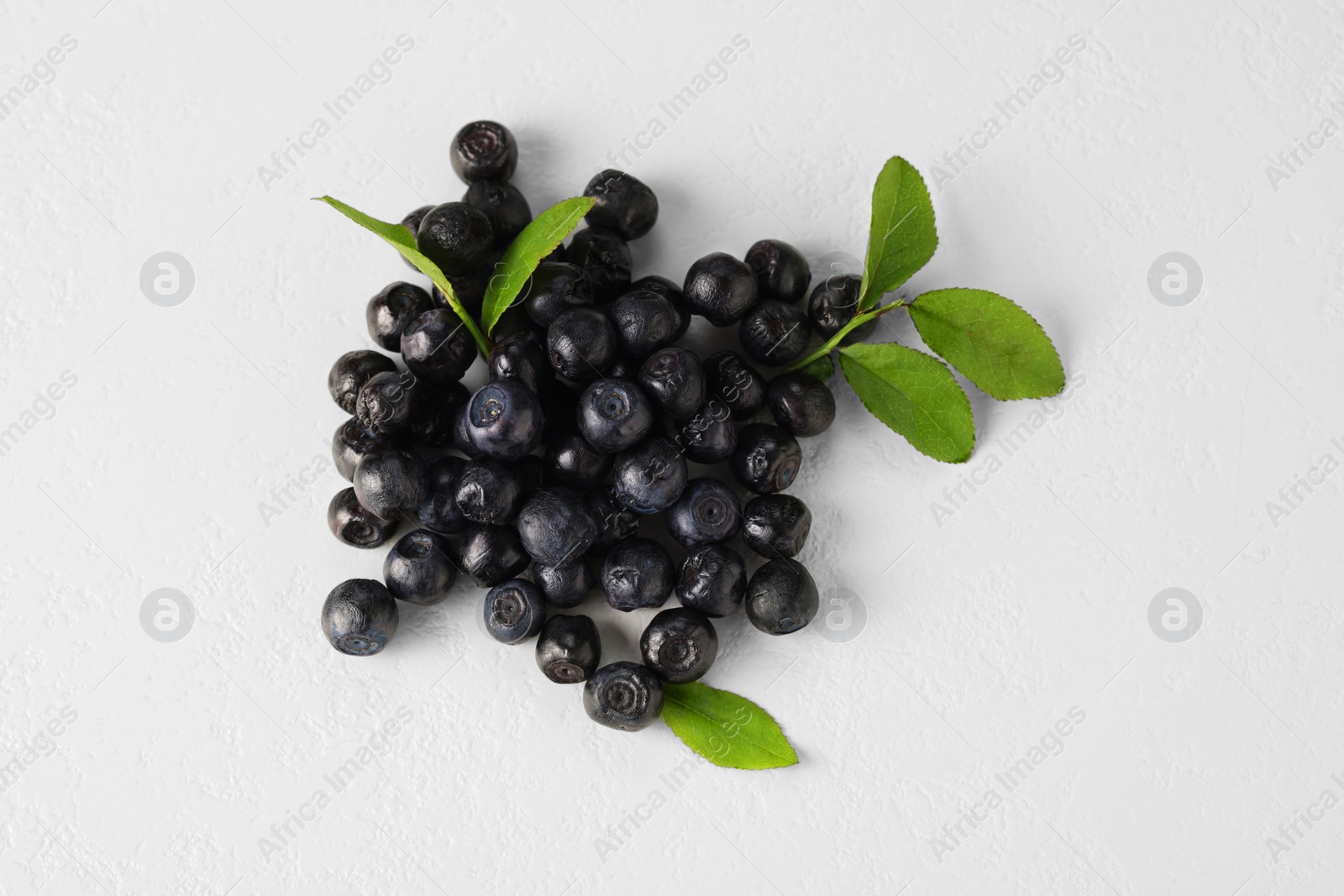 Photo of Pile of ripe bilberries and leaves on white background, flat lay